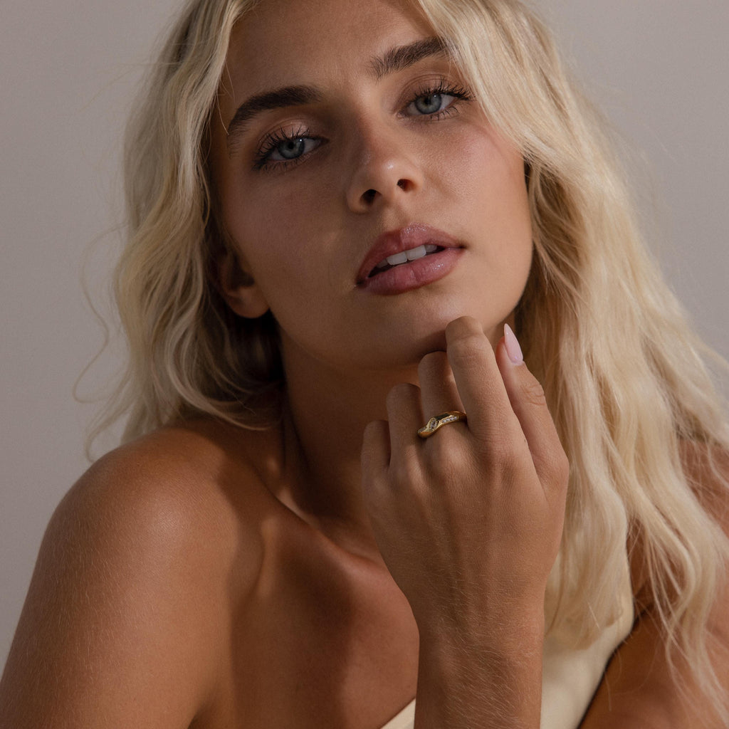 Woman wearing the Radiant Facet Ring in gold with a diamond shaped CZ stone and pave side stones, styled with minimal makeup and a neutral one shoulder top.