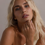 Woman wearing the Radiant Facet Ring in gold with a diamond shaped CZ stone and pave side stones, styled with minimal makeup and a neutral one shoulder top.