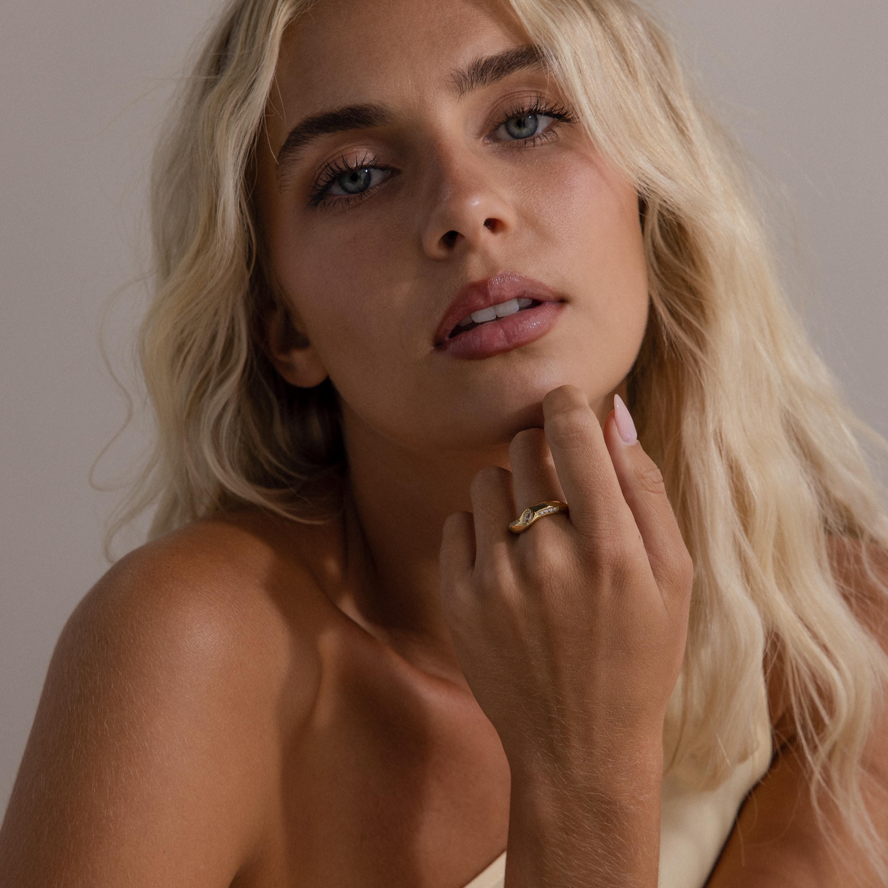 Woman wearing the Radiant Facet Ring in gold with a diamond shaped CZ stone and pave side stones, styled with minimal makeup and a neutral one shoulder top.