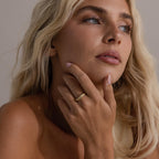Woman wearing the Radiant Facet Ring in gold with a diamond shaped CZ stone and pave set accents, posing with her hand near her face and soft natural makeup.