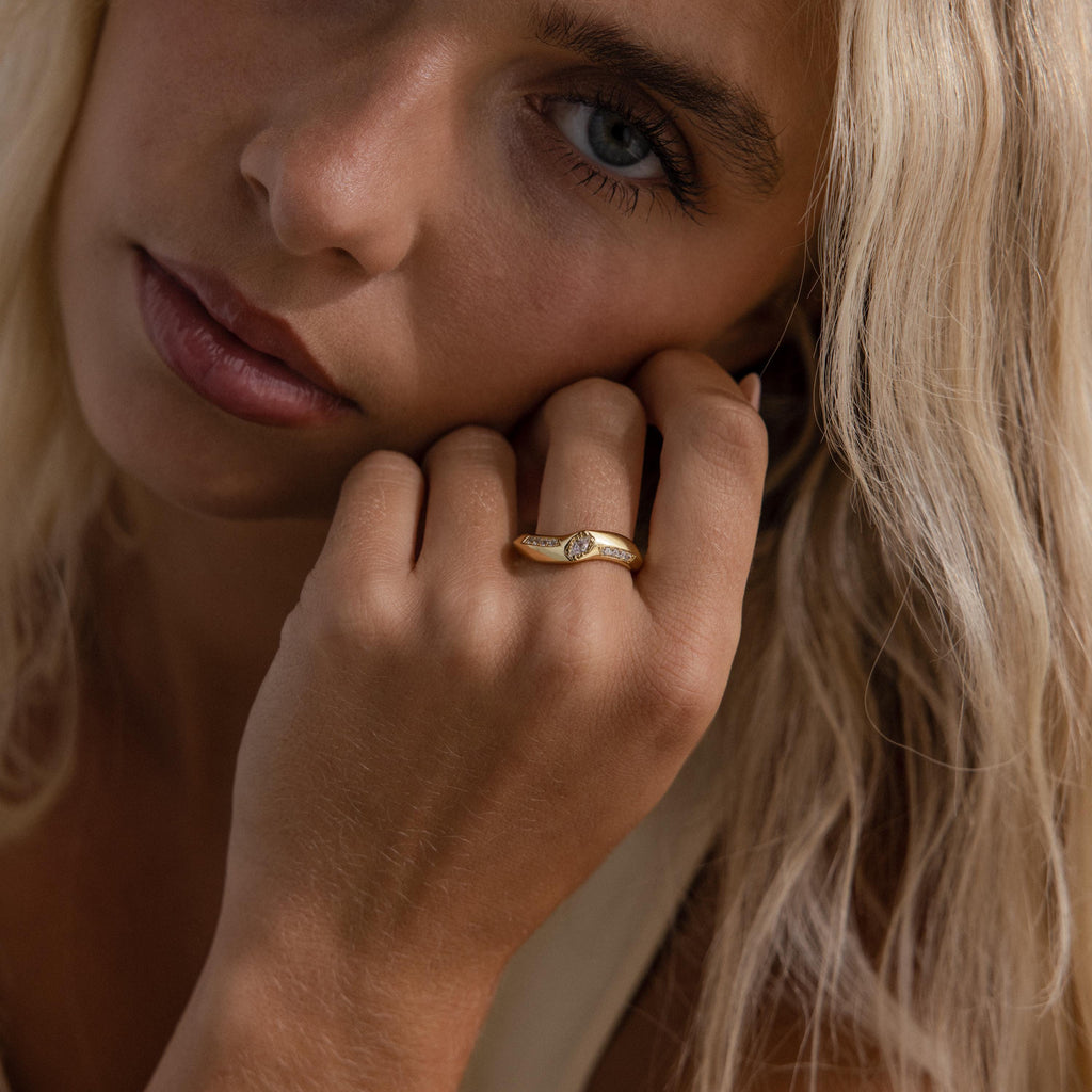 Radiant Facet Ring in polished gold featuring a central diamond shaped CZ stone with tapered band and delicate side stone accents, shown on a woman’s hand.