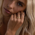 Radiant Facet Ring in polished gold featuring a central diamond shaped CZ stone with tapered band and delicate side stone accents, shown on a woman’s hand.