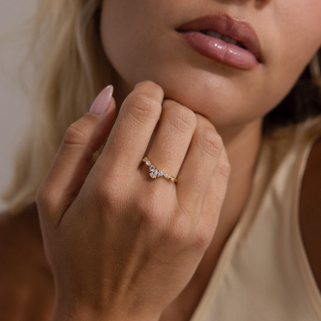 Woman wearing the Radiant Tear Ring in gold with a pear cut diamond center and marquise side stones, shown close up with natural glossy lips and nude nail polish.