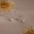 Silver stud earrings with diamond clusters and detachable butterfly shaped drops featuring marquise stones, displayed on a soft neutral surface with flowers.