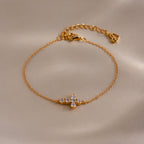Gold chain bracelet with an adjustable clasp, featuring a cross shaped charm set with small round white gemstones.