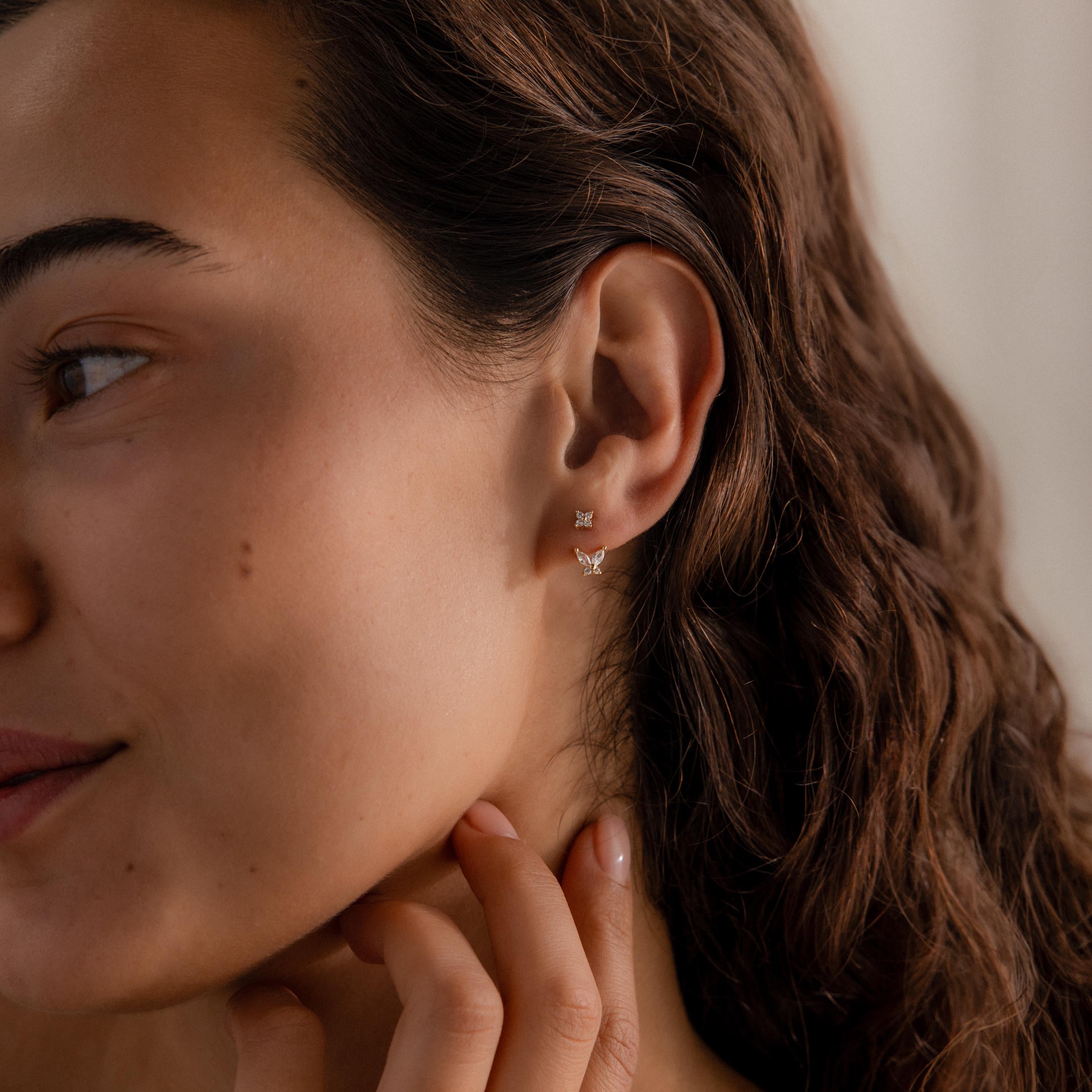 Woman wearing gold stud earrings with diamond clusters and detachable butterfly shaped drops, styled with natural curls and minimal makeup.