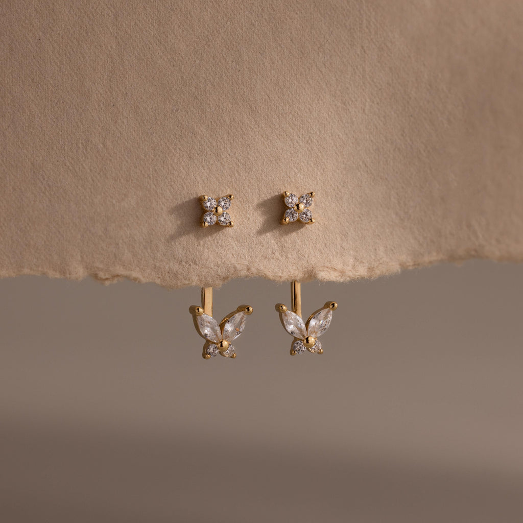 Gold stud earrings with clustered diamonds and detachable butterfly shaped drops featuring marquise and round stones, displayed on textured neutral paper.