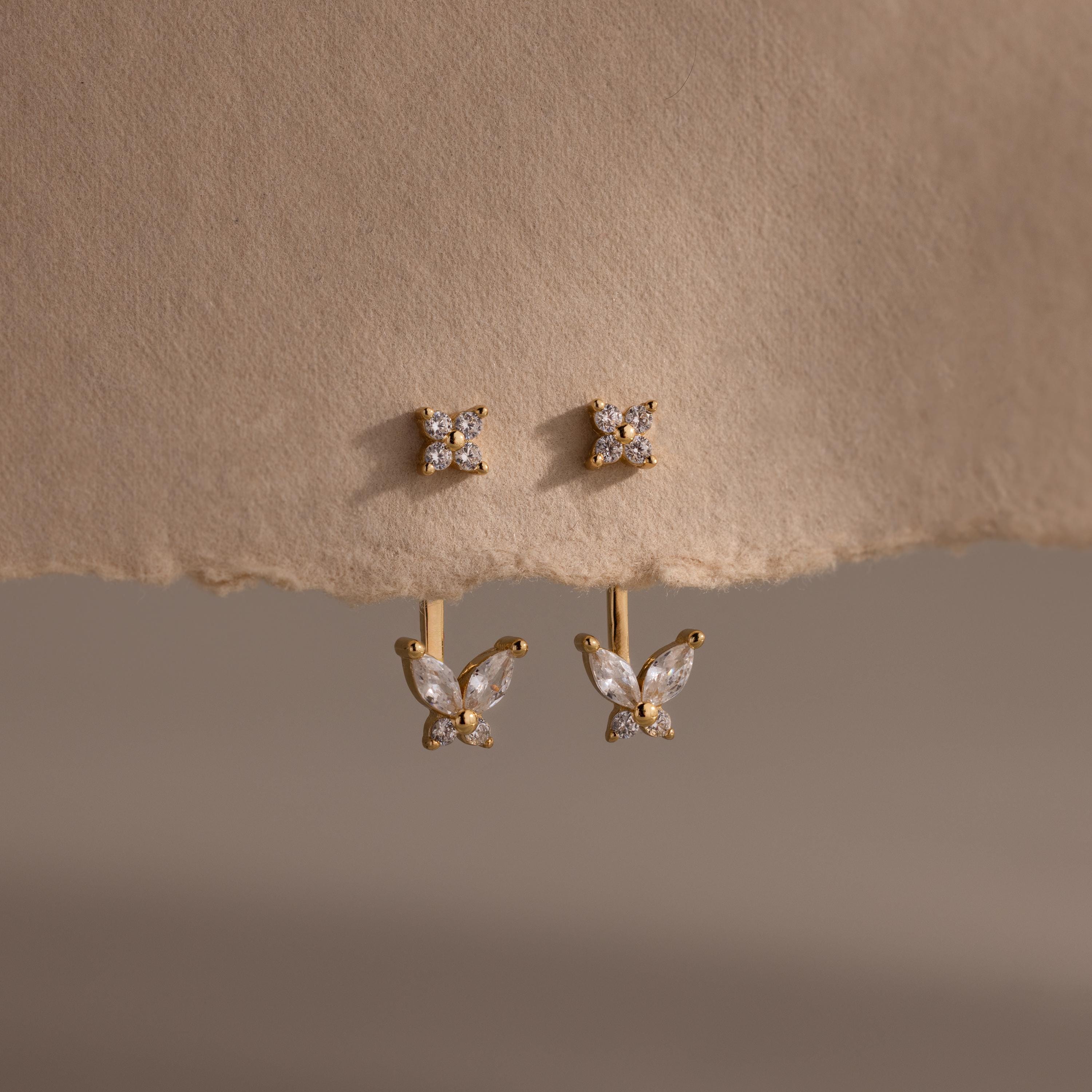 Gold stud earrings with clustered diamonds and detachable butterfly shaped drops featuring marquise and round stones, displayed on textured neutral paper.