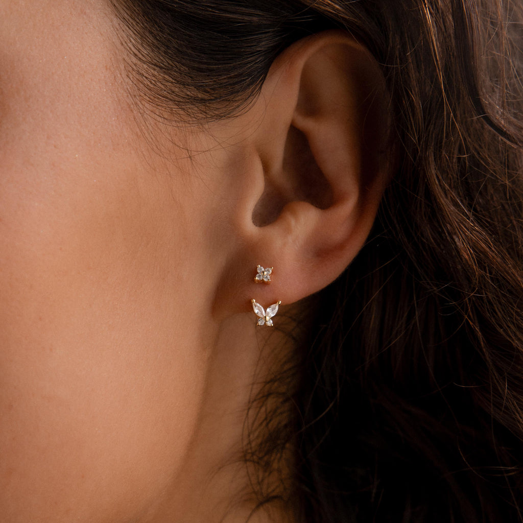 Gold stud earrings with diamond clusters paired with detachable butterfly-shaped drops, worn on the ear for a delicate layered look.