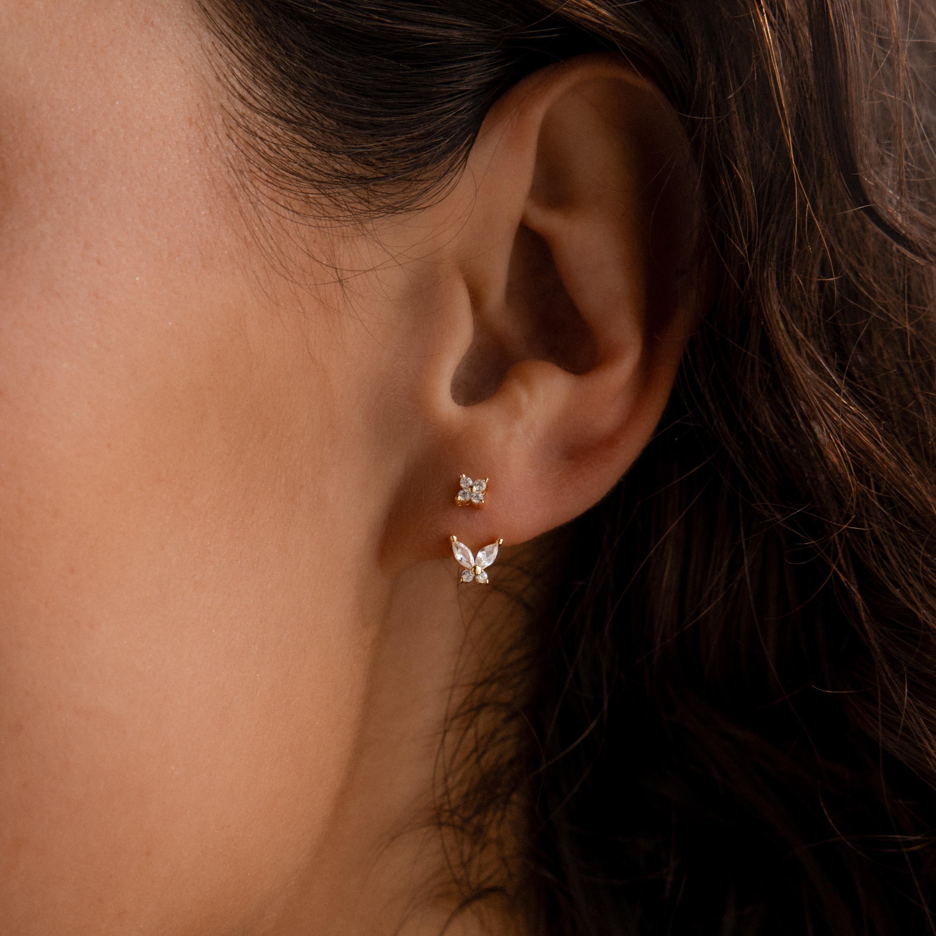 Gold stud earrings with diamond clusters paired with detachable butterfly-shaped drops, worn on the ear for a delicate layered look.