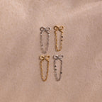 Four Bow Chain Studs in gold and silver feature delicate chain accents. Displayed on beige fabric, these feminine, vintage-inspired earrings are a charming jewelry addition.