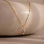 Butterfly Drop Necklace, featuring three small sparkling diamonds, is displayed on a smooth beige surface—an elegant piece of nature-inspired jewelry.