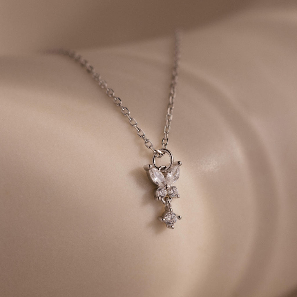 The Butterfly Drop Necklace in Sterling Silver features a delicate, sparkling pendant inspired by nature, elegantly resting on smooth, light-colored skin.