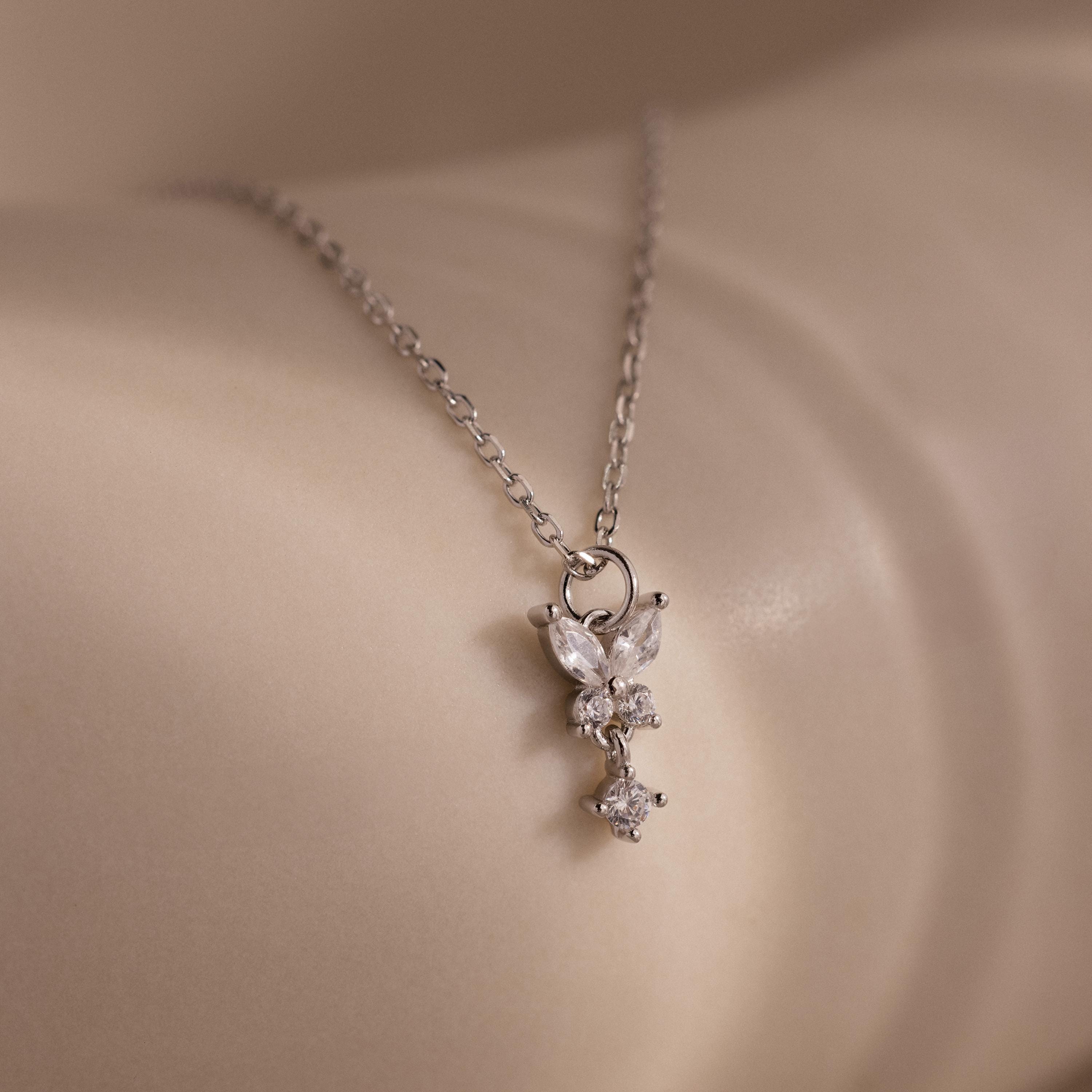 The Butterfly Drop Necklace in Sterling Silver features a delicate, sparkling pendant inspired by nature, elegantly resting on smooth, light-colored skin.