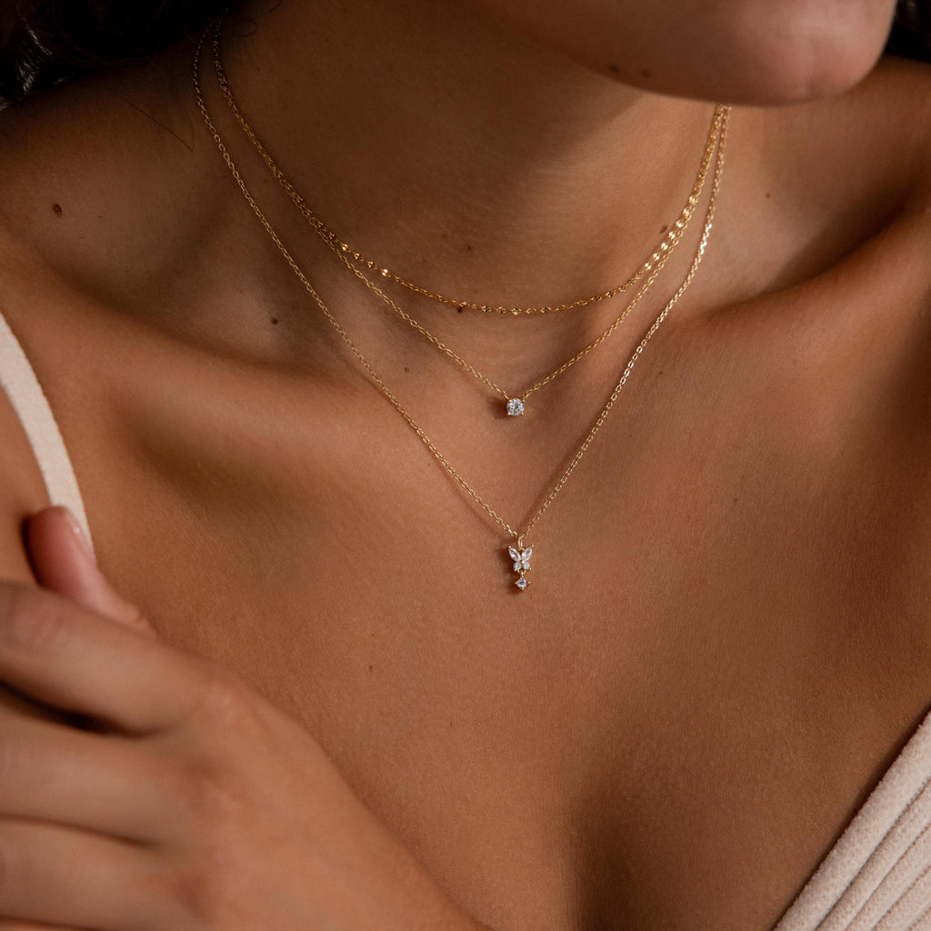 A woman shown from the shoulders up wears layered gold necklaces, featuring the Butterfly Drop Necklace—a delicate gold chain adorned with butterfly pendants.