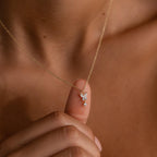 A hand displays the Butterfly Drop Necklace in 18K Gold, its small, delicate gold pendant resting against bare skin—a stunning piece of nature-inspired jewelry.