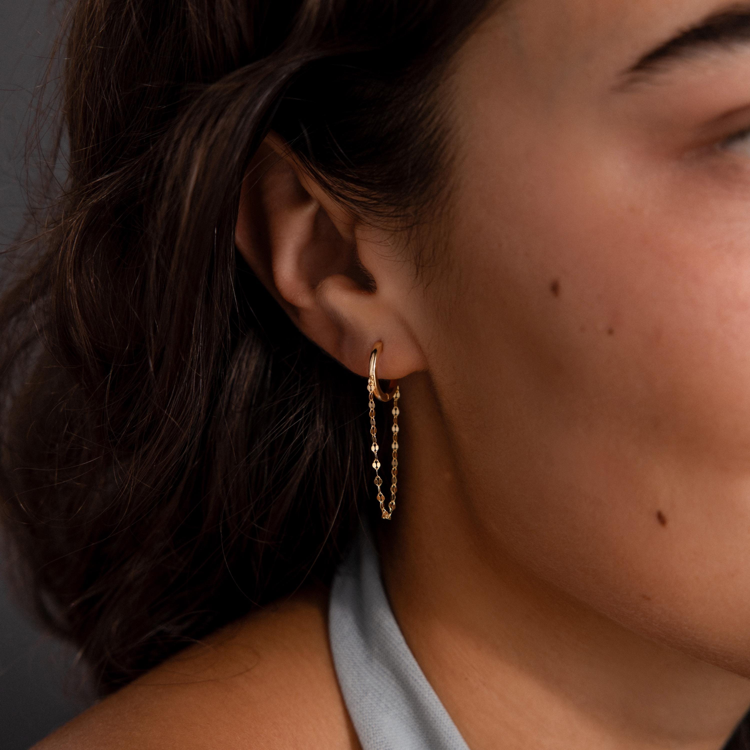 Close-up of a person wearing Mirror Chain Huggies in 18K Gold—a minimalist gold hoop earring with a delicate chain accent, ideal for lovers of simple, elegant jewelry.