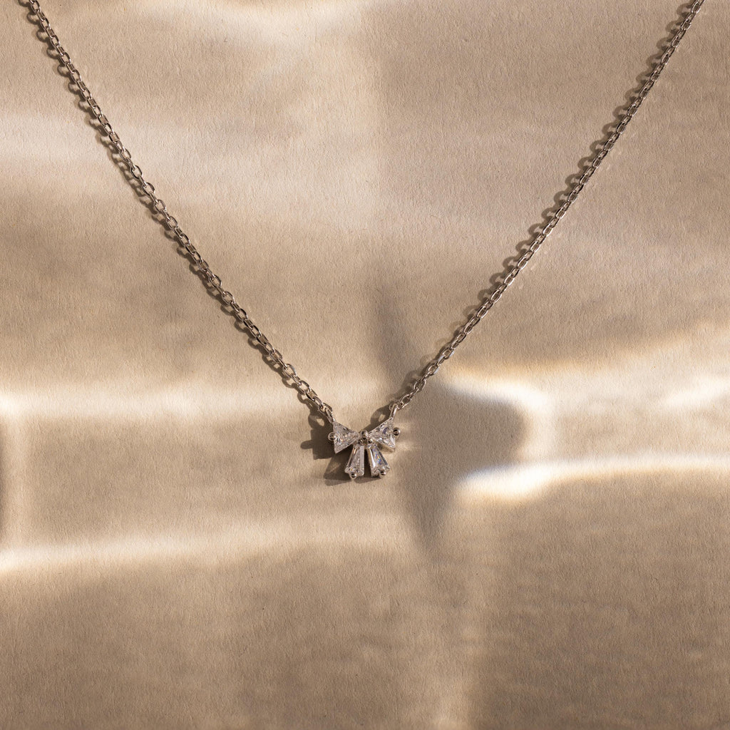 Diamond Bow Necklace in Sterling Silver, elegantly displayed on a softly lit beige background.