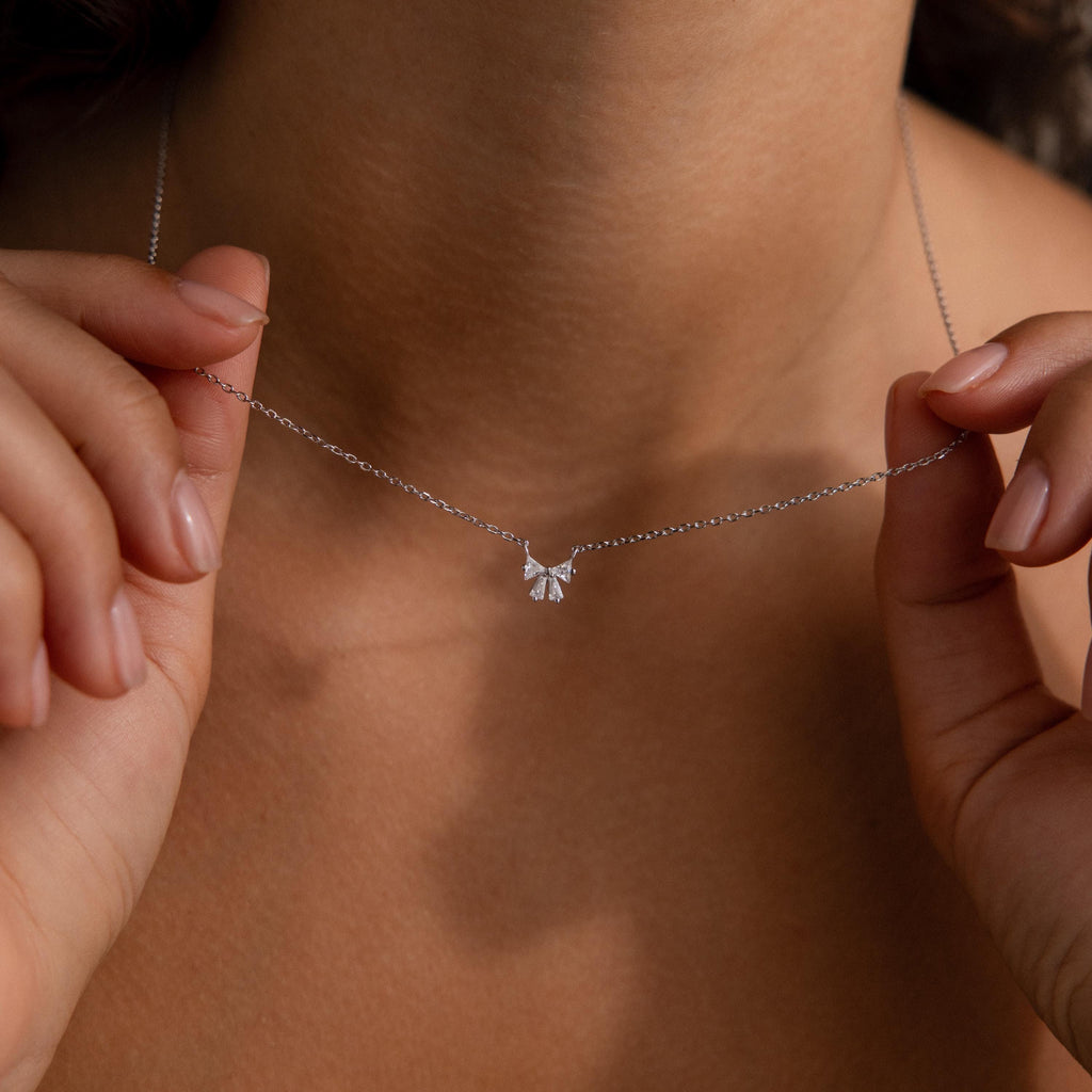 Close-up of a person holding the Diamond Bow Necklace in Sterling Silver, featuring a sparkling bow pendant around their neck.