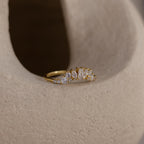 The Diamond Curve Cluster Ring is displayed on a light, textured surface, showcasing its unique design with multiple small, baguette, round & marquise shaped clear gemstones.