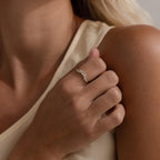 A person with light skin touches their collarbone while wearing the Diamond Curve Cluster Ring, featuring several small clear gemstones in different shapes on their ring finger.