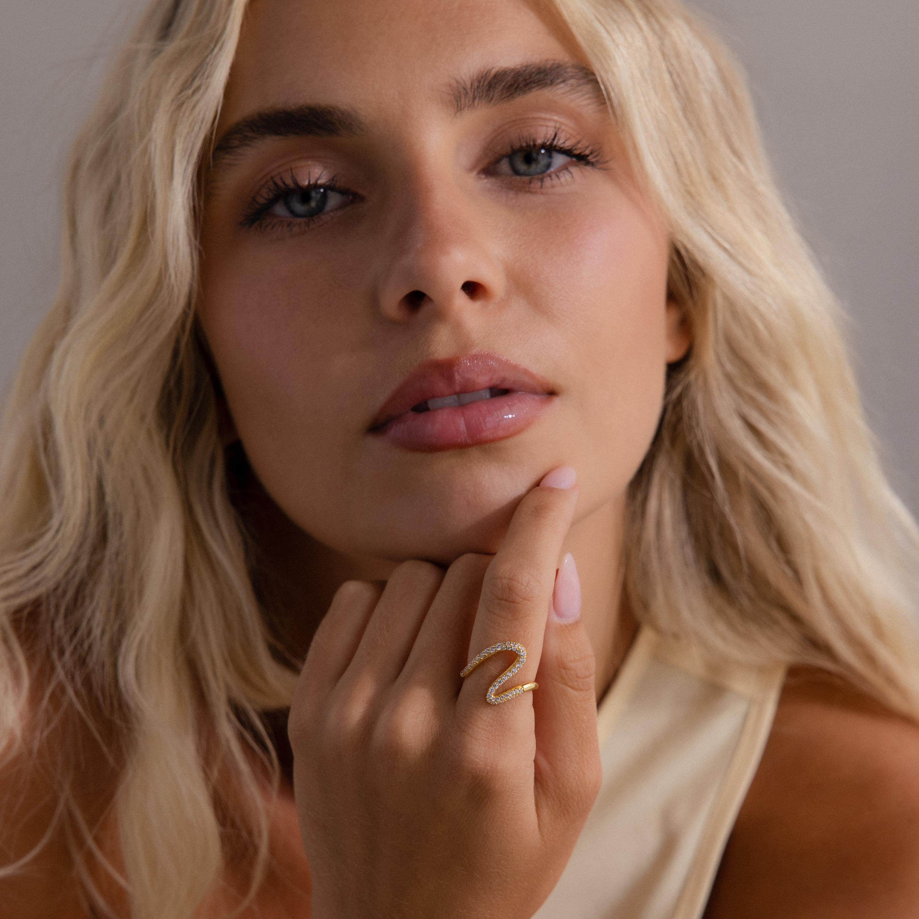 A woman with wavy blonde hair wears the Pave Wave Ring, touching her chin and looking at the camera.