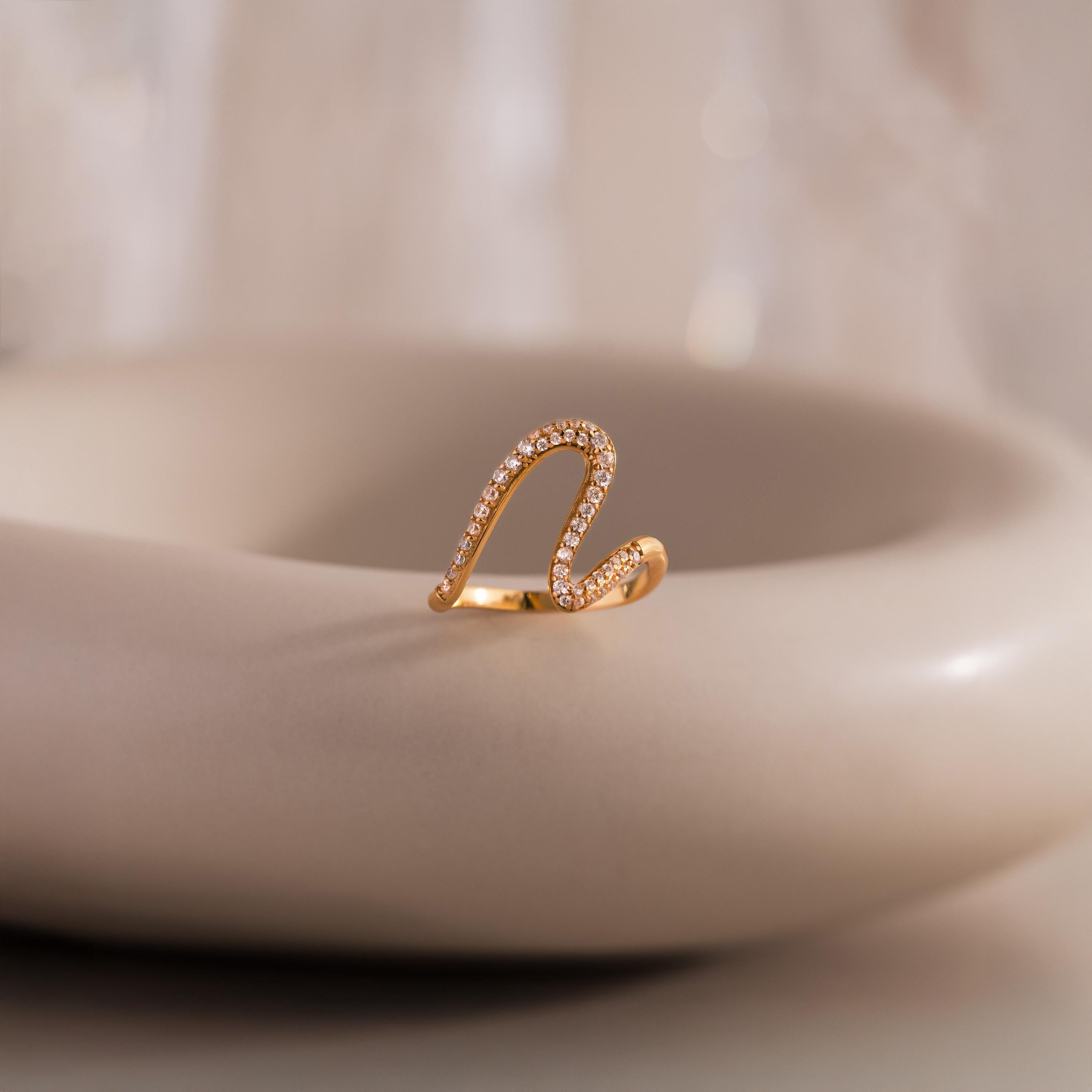 The Pave Wave Ring features a wave-like design with small diamonds, ideal for stacking, shown on a smooth, light-colored surface.