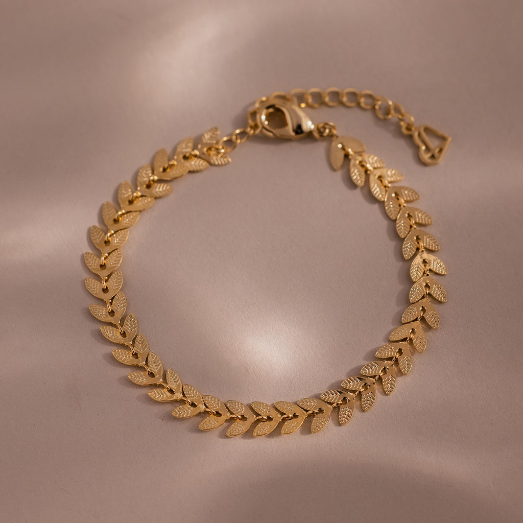 Flat-lay of a gold leaf link chain bracelet with textured leaf-shaped links displayed on a neutral surface.