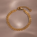 Flat-lay of a gold leaf link chain bracelet with textured leaf-shaped links displayed on a neutral surface.
