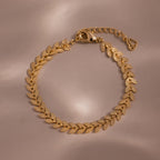 Flat-lay of a gold leaf link chain bracelet with textured leaf-shaped links displayed on a neutral surface.