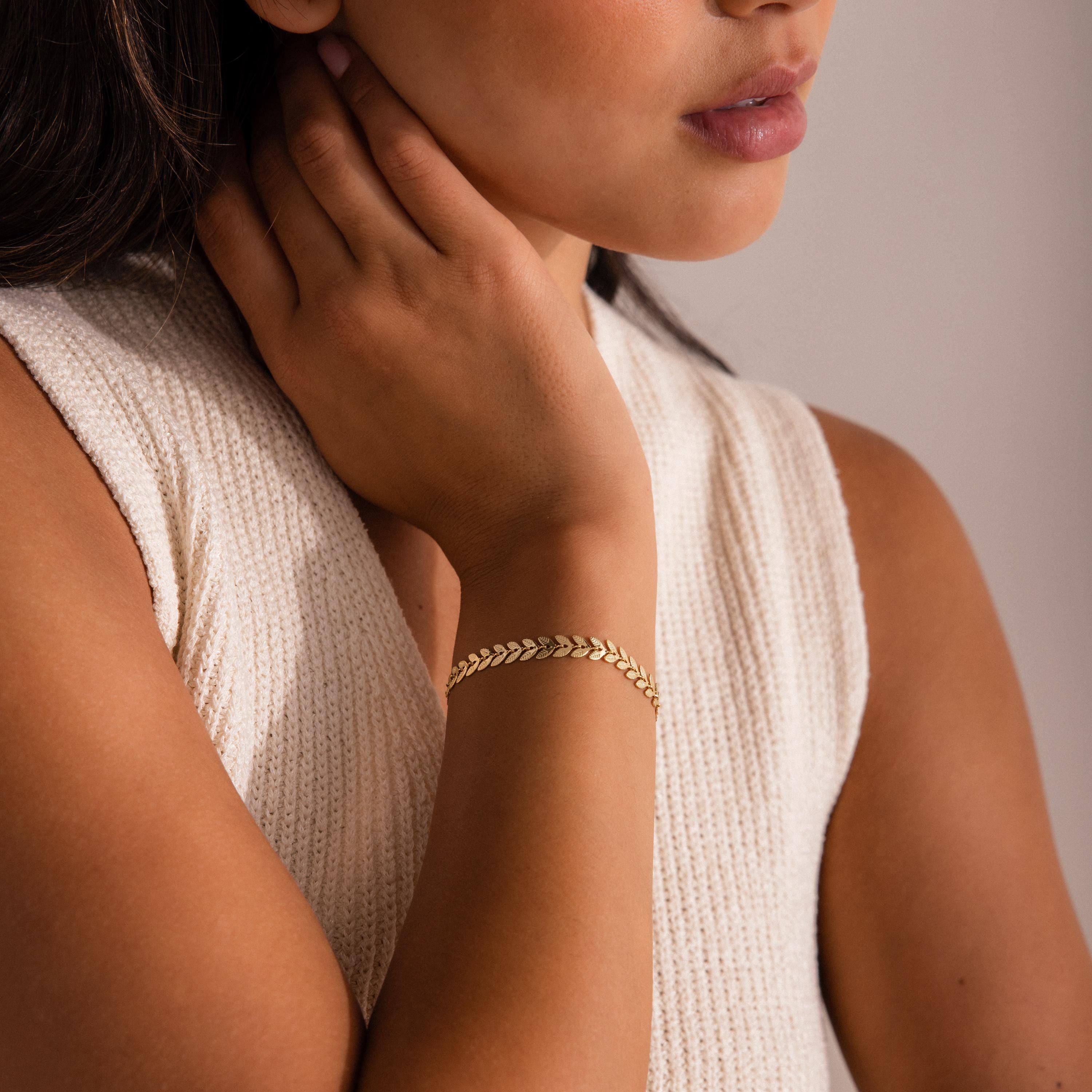 Woman wearing a sleeveless knit top and the Leaf Link Bracelet, with her hand touching her neck.