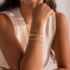 Model wearing a gold leaf link chain bracelet, stacked with two dainty gold link chain bracelets.