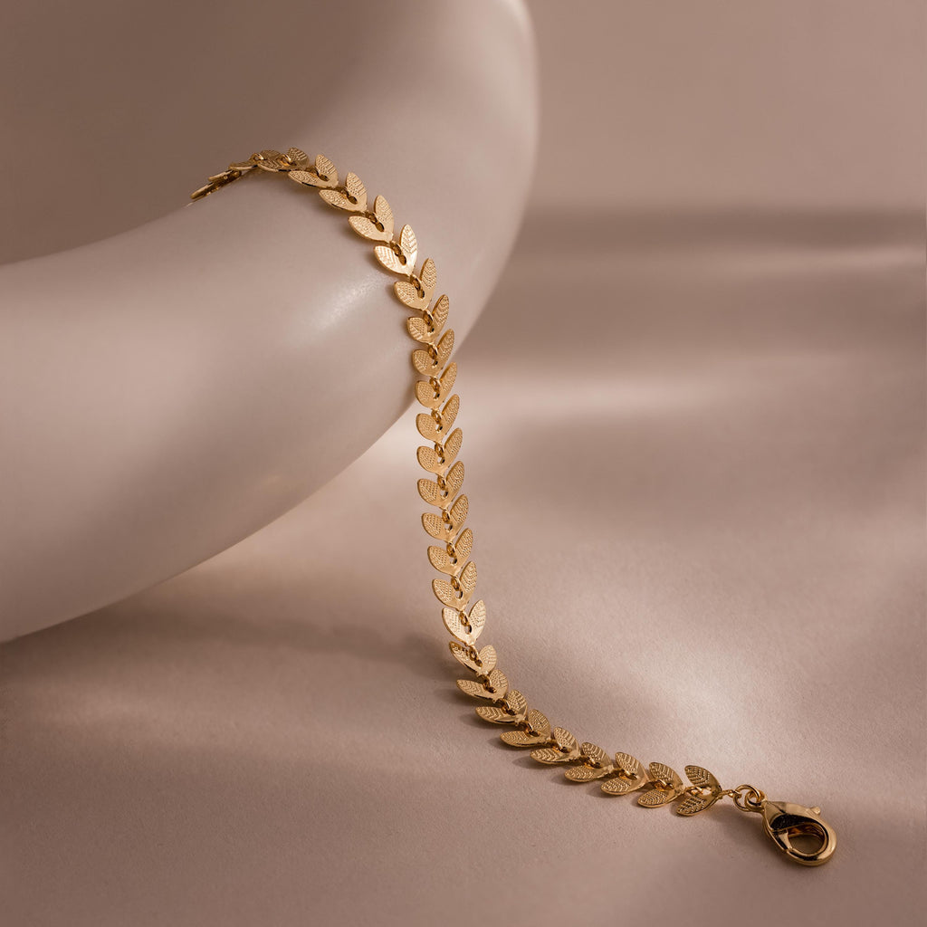 Close-up of a gold leaf link chain bracelet with textured leaf-shaped links displayed on a ceramic dish.