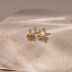 Bow Drop Studs are elegant earrings featuring small gemstones. Beautifully displayed on a textured light stone surface.