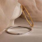 Skinny Diamond Bangle in gold and silver, featuring small diamonds and minimalist design, displayed on a light surface with a soft beige fabric background.