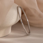 The Skinny Diamond Bangle in White Gold features a simple design with a small diamond accent, shown on a smooth, light-colored stone.