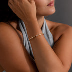 A woman wearing a sleeveless gray top and the Skinny Diamond Bangle—a minimalist gold bracelet featuring a small cubic zirconia gemstone.