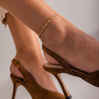 Close-up of a gold chain bracelet with white pearls set in oval links, displayed against a soft neutral fabric background.