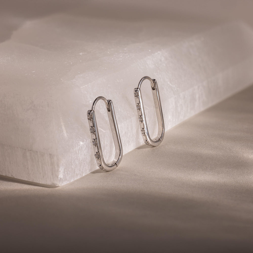 These Dainty Pave Link Earrings, featuring a minimalist design, are displayed on a white stone slab under soft, diffused lighting.