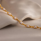 Close-up of a gold chain bracelet with white pearls set in oval links, displayed against a soft neutral fabric background.