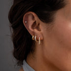 Close-up of a woman’s ear wearing four minimalist earrings, including Dainty Pave Link Earrings in 18K Gold, a small stud, and two elegant gold hoops.