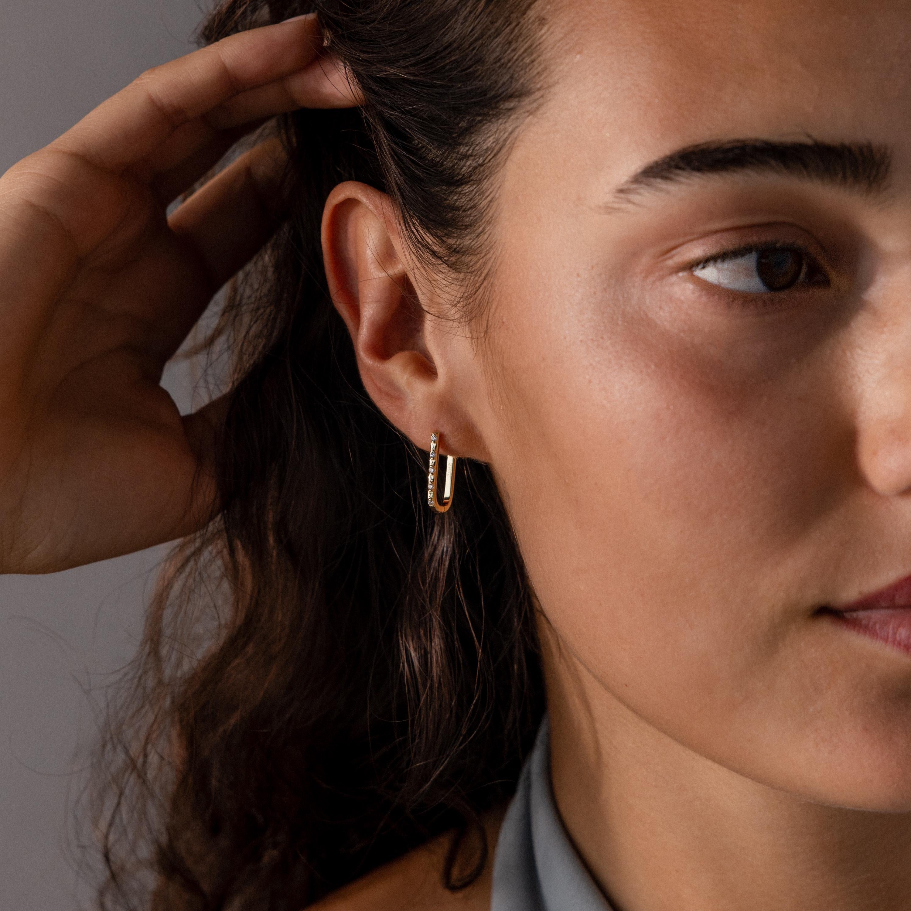 Woman with dark wavy hair wearing Dainty Pave Link Earrings in 18K Gold, photographed in soft lighting.