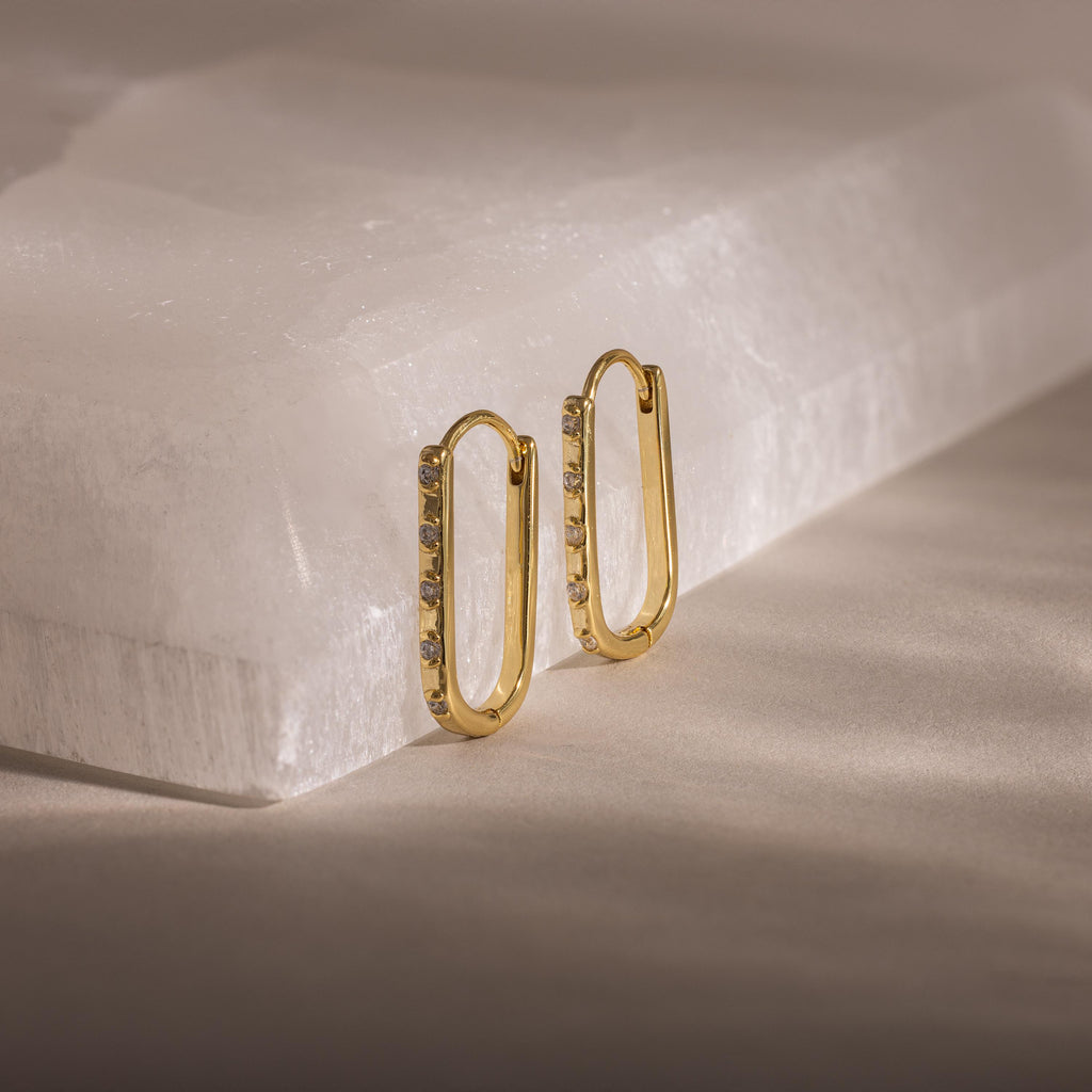 Dainty Pave Link Earrings—gold rectangular hoops with cubic zirconia, shown on a white stone surface in soft light. These minimalist earrings add subtle sparkle to any look.