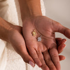 Gold and silver shell-inspired charm pendants with textured circular designs and gemstone accents, displayed in the palm of a hand.