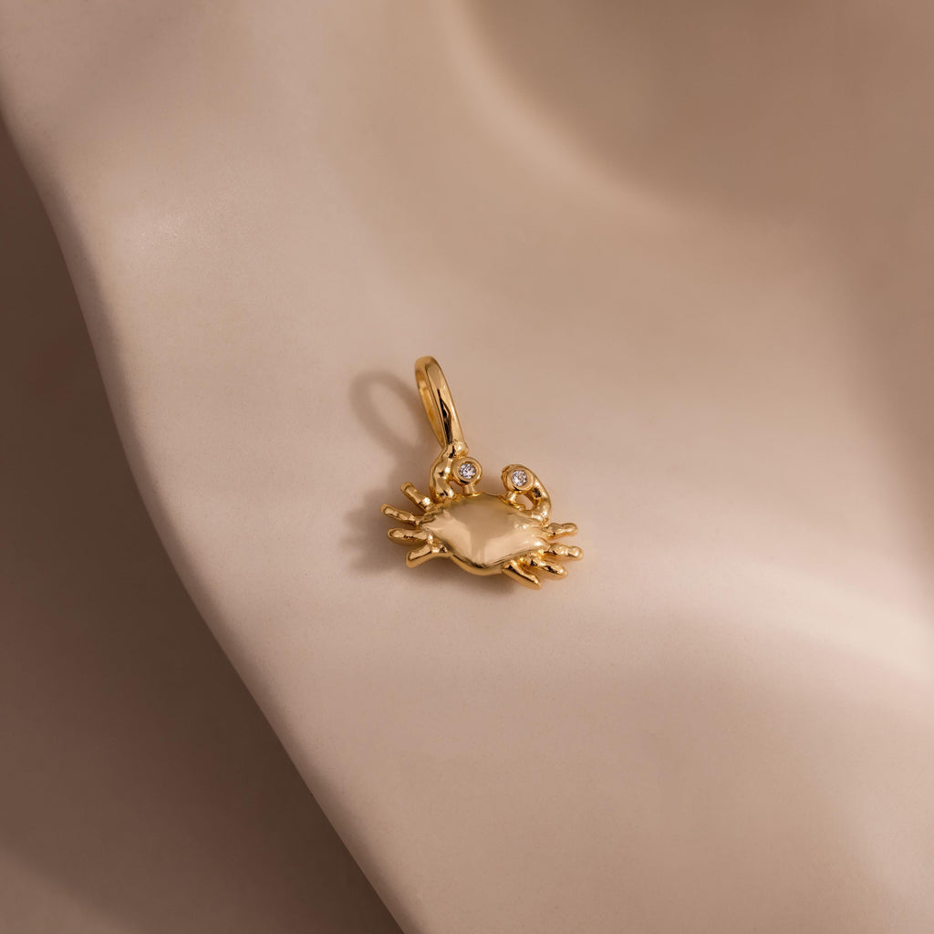Gold crab charm pendant with sparkling gemstone eyes, displayed on a soft neutral background.