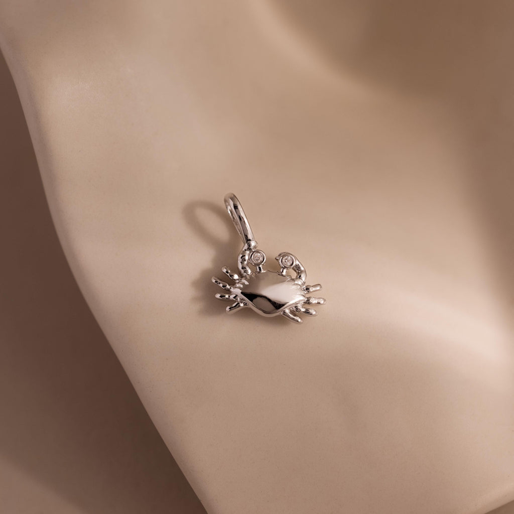 Silver crab charm pendant with gemstone eyes, displayed on a soft neutral background.