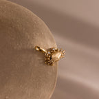 Gold crab shaped charm pendant with gemstone accented eyes, displayed on a smooth stone surface against a neutral background.
