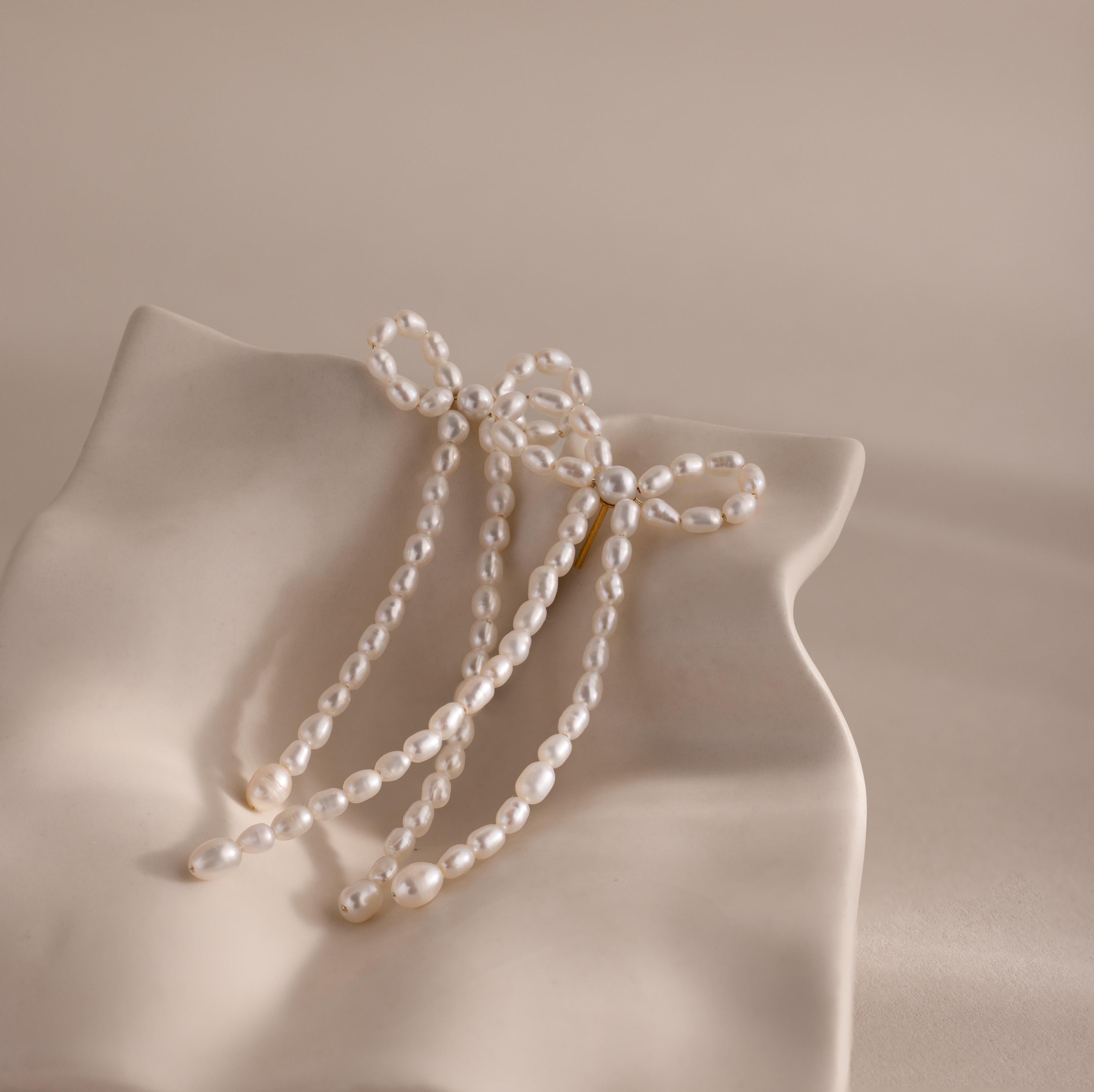 Elegant and chic, the Pearl Bow Earrings feature delicate bows with dangling pearls, making them a perfect statement piece—beautifully displayed on a wavy, cream-colored ceramic dish.