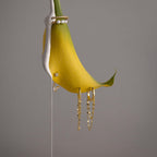 A yellow flower petal adorned with pearls and Duo Mirror Chain Huggies in 18K Gold hangs elegantly against a plain gray background.