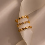 Set of three eternity curve rings in gold, featuring quilted wave design with one band accented by sparkling diamonds, displayed on soft ivory fabric.